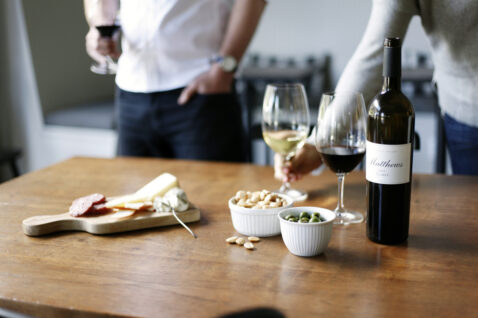 A wood table of red and white wine glasses, charcuterie, almonds and olives