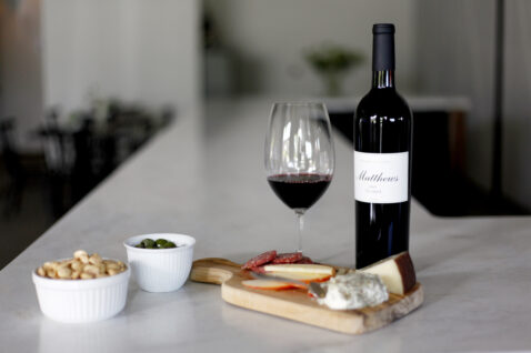 A bottle of 2013 Claret on the marble bar top with a glass of red, a charcuterie board and almond snacks