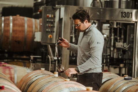 Winemaker Aryn Morell pulling a red wine sample out of a barrel and filling a glass