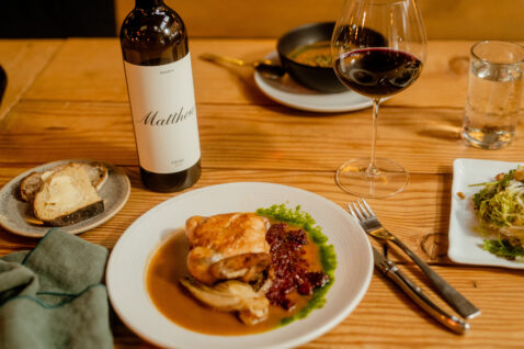 Table setting with roasted chicken, bread and butter, full wine glass and 2018 Reserve Cuvee bottle