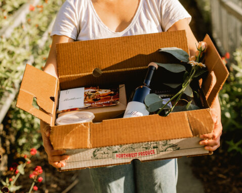 Woman in white shirt holding a Matthews meal kit full of goods and wine