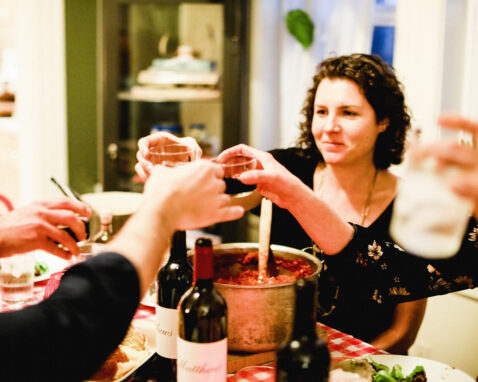 People cheersing at a dining room table with Pasta and Matthews wine bottles