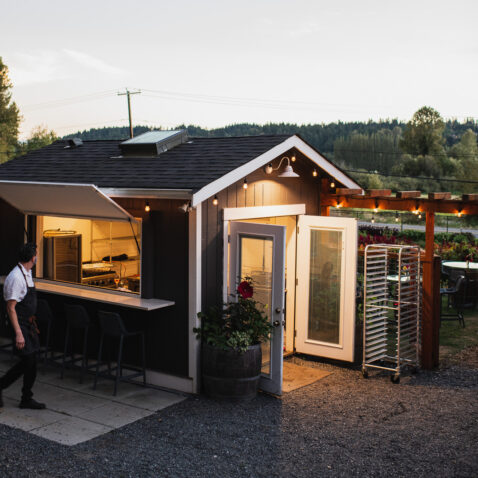 Matthews farm kitchen at dusk with doors and windows open and the lights inside glowing