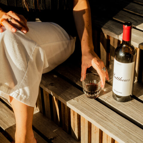 Close up of Reserve Cabernet Franc bottle on stairs with woman holding a glass full of wine