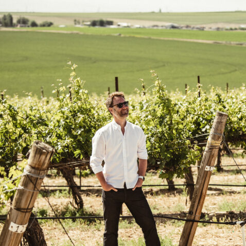Owner Bryan Otis standing in front of vines looking off in the distance