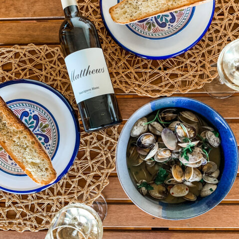 Looking down on a bowl of fresh clams, grilled baguette and a bottle of Sauv Blanc
