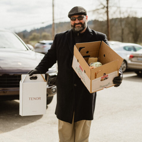 Matthews employee carrying a farm box full of produce and a carry case of Tenor wines