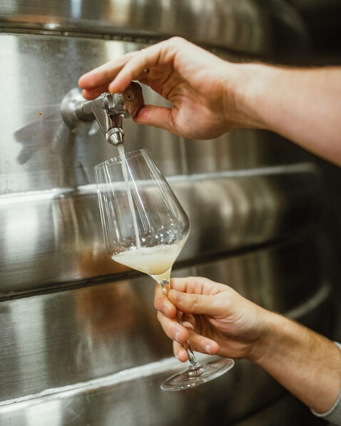Hand holding a wine glass, opening a tank spout and pouring in white wine