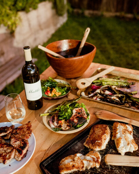 Tablescape of fresh grilled veggies, grilled chicken, salad and a bottle of Matthews Sauv Blanc