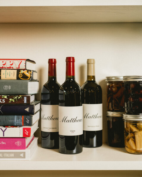 Matthews Claret, Cab Sauv and Sauv Blanc bottles places on a shelf with a stack of books to the left and canned goods to the right
