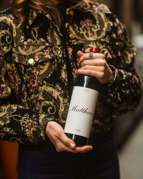 Woman wearing patterned jacket holding a bottle of 2018 Reserve Cuvee