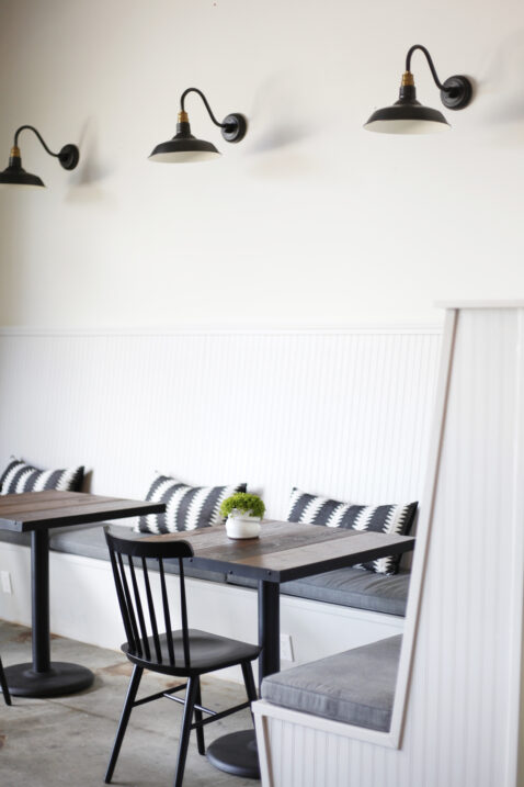 Tasting room banquette with grey cushions, stripped pillows and black farm house lights above