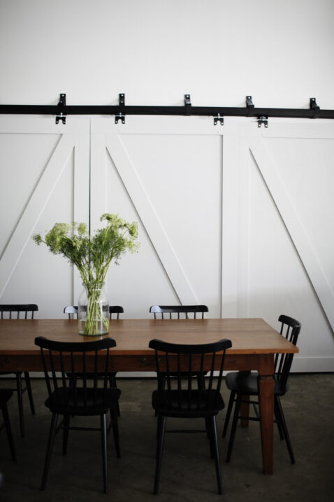 Large wood table and black chairs, green center arrangement, and white sliding farm doors in the background