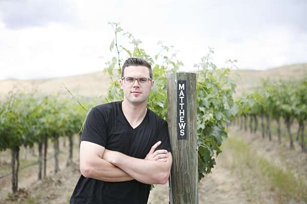 Winemaker Aryn Morell leaning against a vineyard post labeled Matthews