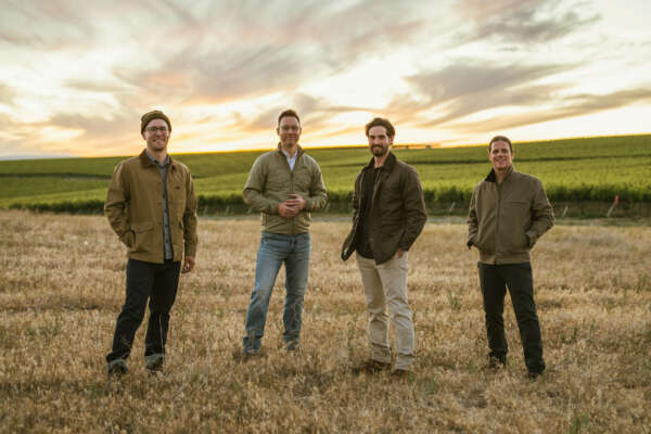 Three winemakers and owner Bryan Otis standing in field with vineyards behind