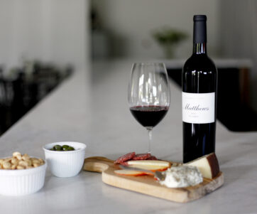 A bottle of 2013 Claret on the marble bar top with a full glass and cheese board