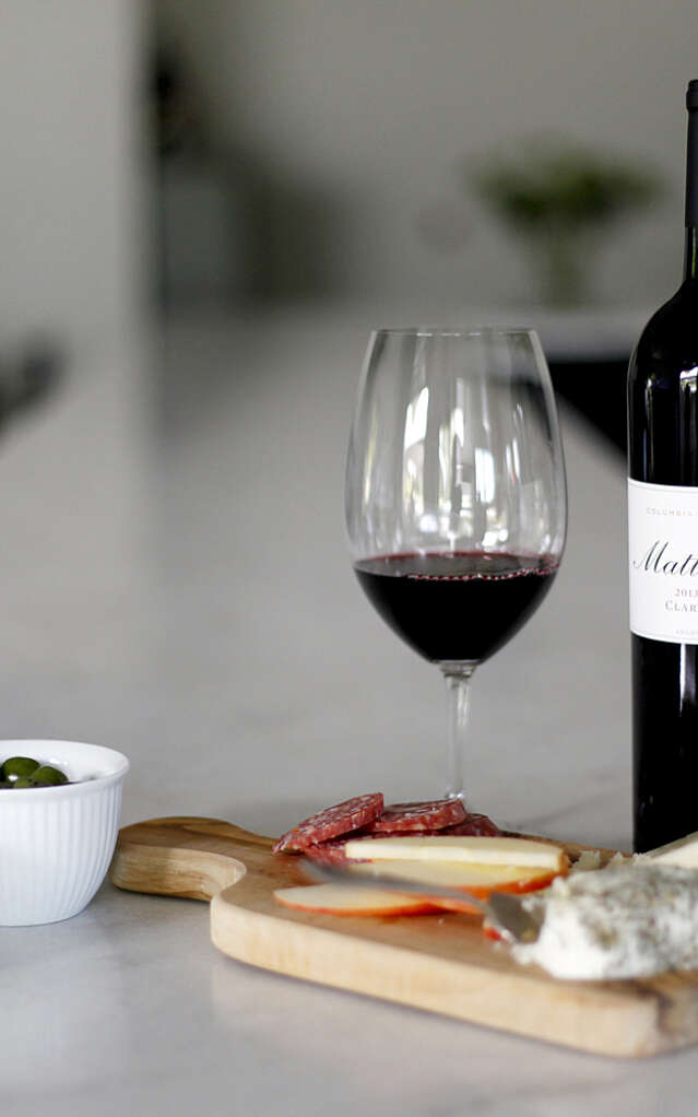 A bottle of 2013 Claret on the marble bar top with a full glass and cheese board
