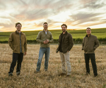 Three winemakers and owner Bryan Otis standing in field with vineyards behind
