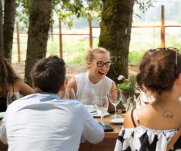 A group of people seated at a long table outside with a blonde women laughing on the other side of the table