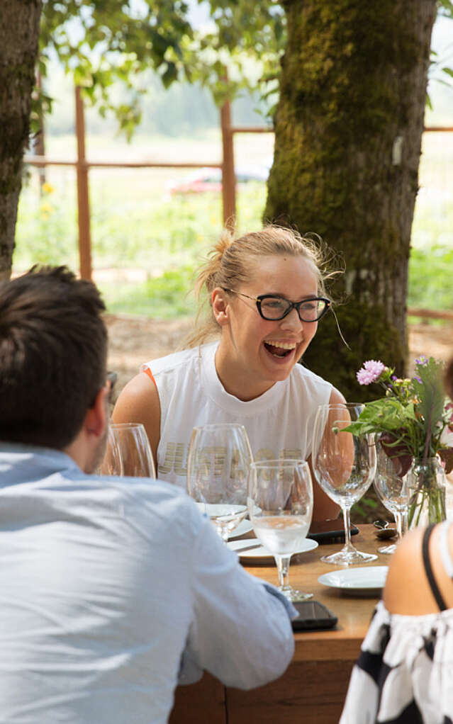A group of people seated at a long table outside with a blonde women laughing on the other side of the table